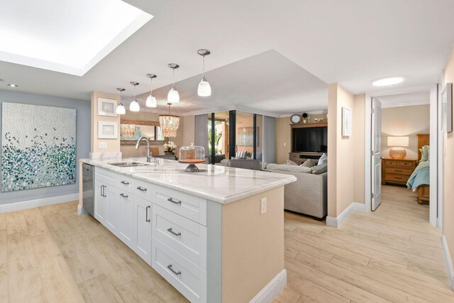 kitchen with light stone counters, a sink, dishwasher, white cabinetry, and light wood-type flooring