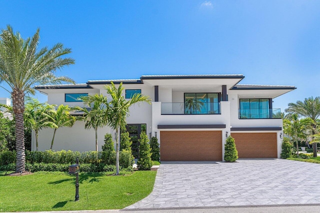 contemporary home featuring stucco siding, a garage, a front yard, and a balcony