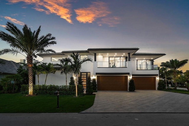 modern home featuring a balcony, an attached garage, stucco siding, a front yard, and driveway