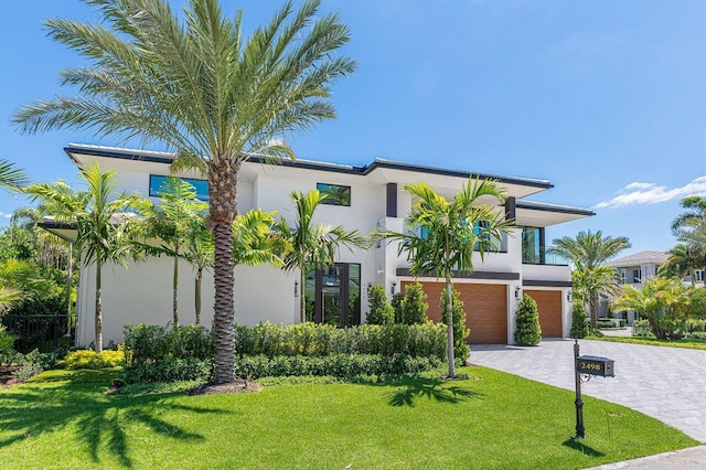 contemporary home featuring stucco siding, a garage, decorative driveway, and a front yard