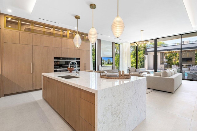 kitchen with modern cabinets, a sink, expansive windows, open floor plan, and light stone counters