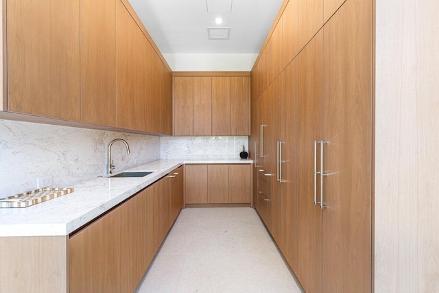 kitchen with a sink, tasteful backsplash, modern cabinets, brown cabinetry, and light stone countertops