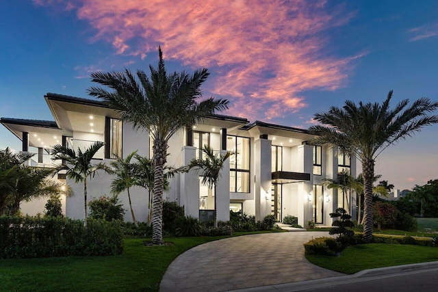 view of front of house featuring stucco siding, curved driveway, and a front lawn