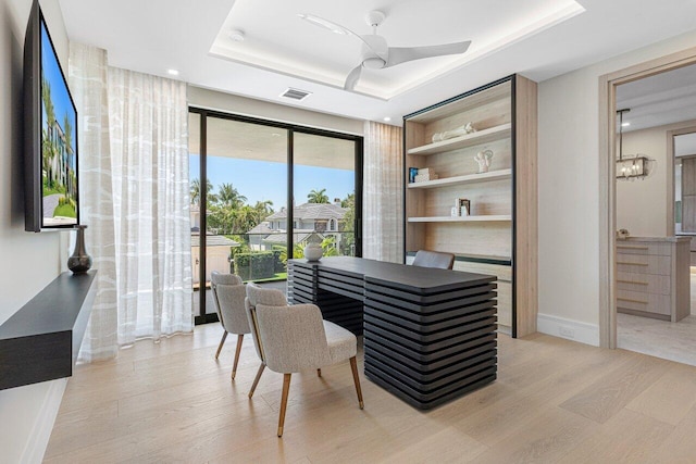 office with light wood-style floors, a tray ceiling, ceiling fan, and baseboards
