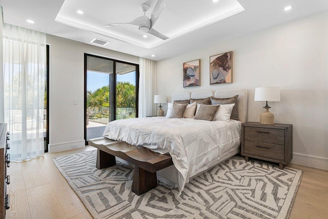 bedroom featuring access to outside, a raised ceiling, light wood-style flooring, recessed lighting, and baseboards