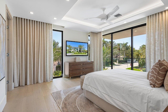 bedroom featuring a tray ceiling, access to exterior, light wood-style floors, multiple windows, and recessed lighting