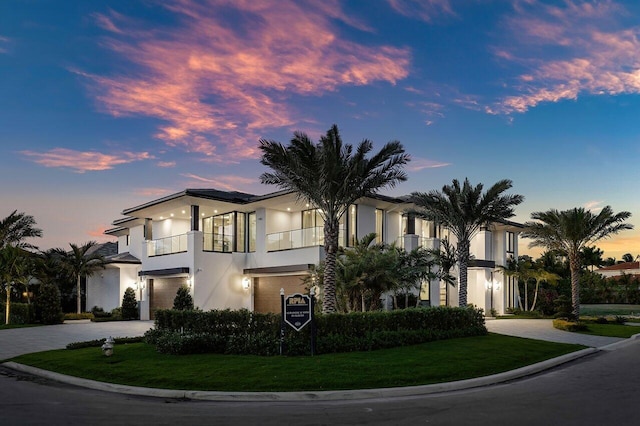 view of front facade featuring curved driveway, a balcony, stucco siding, and a yard