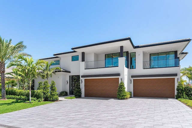 contemporary house with stucco siding, a balcony, an attached garage, and decorative driveway