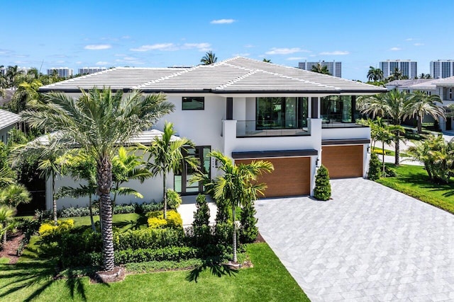 view of front of house with a garage, a balcony, decorative driveway, stucco siding, and a tile roof