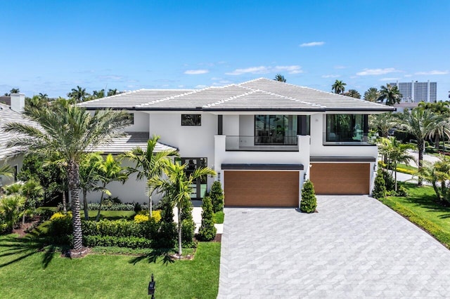 contemporary house with a balcony, stucco siding, an attached garage, a front lawn, and decorative driveway