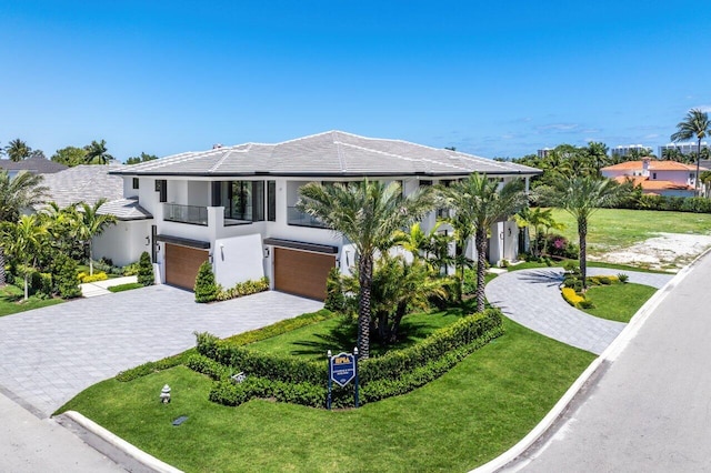 contemporary house featuring an attached garage, decorative driveway, a front lawn, and a balcony