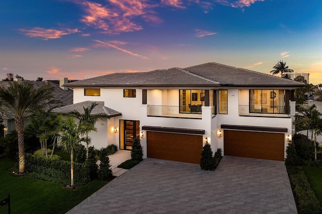 view of front facade with stucco siding, a balcony, a garage, and decorative driveway