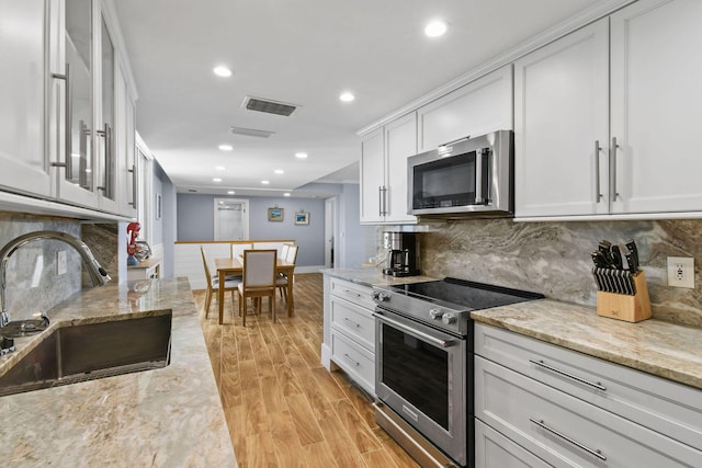 kitchen with appliances with stainless steel finishes, a sink, light wood-style floors, recessed lighting, and light stone counters