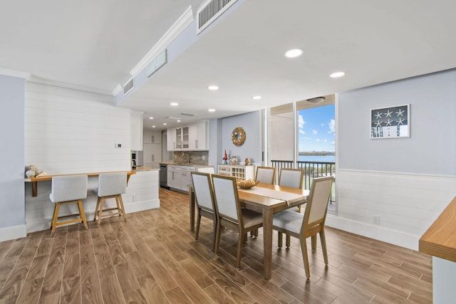 dining room featuring wood finished floors, a water view, recessed lighting, and ornamental molding