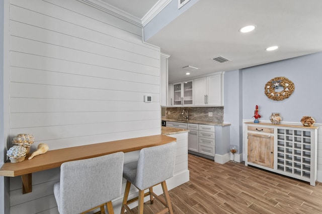 kitchen with a sink, ornamental molding, glass insert cabinets, white cabinetry, and light stone counters