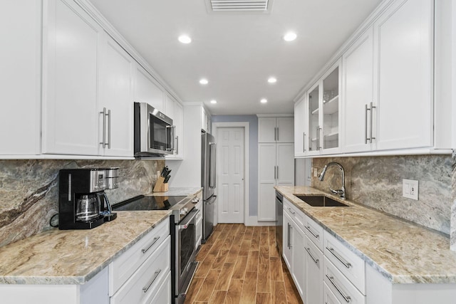 kitchen featuring high end appliances, a sink, recessed lighting, white cabinets, and glass insert cabinets