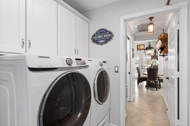 clothes washing area featuring washing machine and clothes dryer, light tile patterned floors, and cabinet space