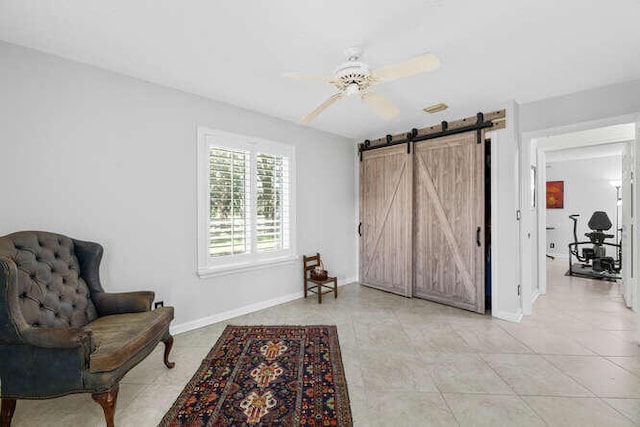 sitting room with baseboards, a barn door, ceiling fan, and light tile patterned flooring