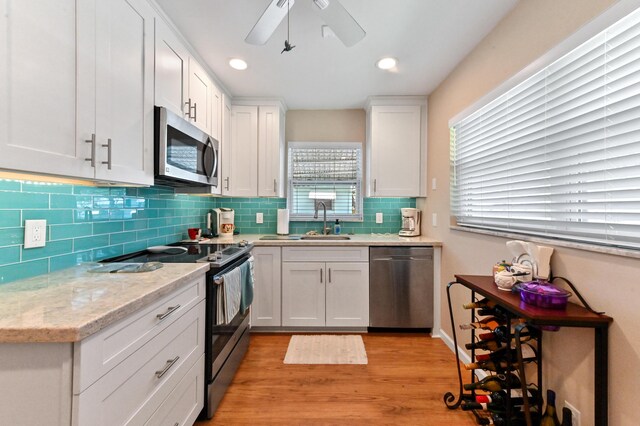 kitchen featuring decorative backsplash, light wood-type flooring, a sink, white cabinets, and stainless steel appliances