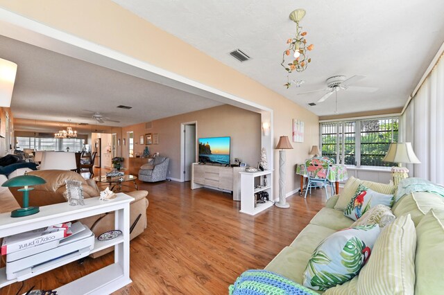 living room featuring baseboards, ceiling fan with notable chandelier, wood finished floors, and visible vents