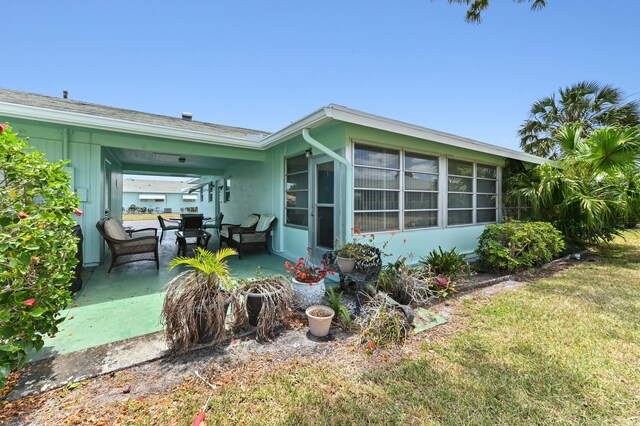 rear view of house featuring a sunroom, a patio area, a yard, and a carport