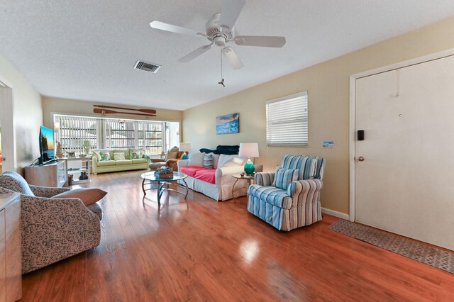 living area with baseboards, a ceiling fan, wood finished floors, and visible vents
