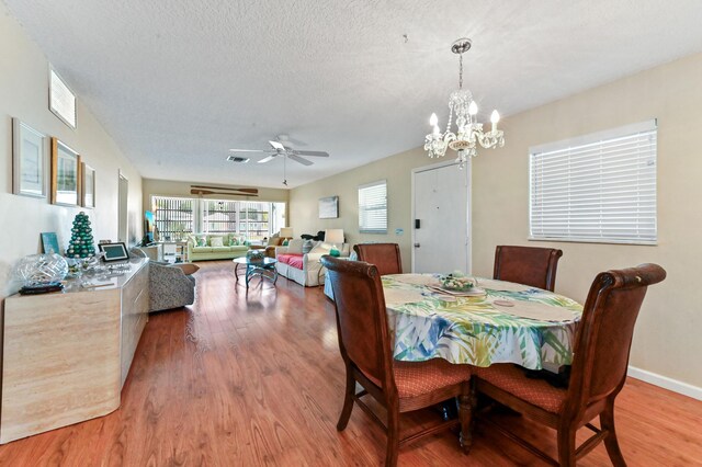 dining room featuring a textured ceiling, ceiling fan with notable chandelier, baseboards, wood finished floors, and visible vents