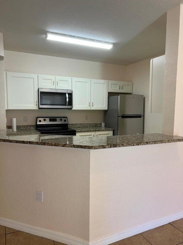 kitchen featuring appliances with stainless steel finishes, dark stone countertops, a peninsula, and white cabinets