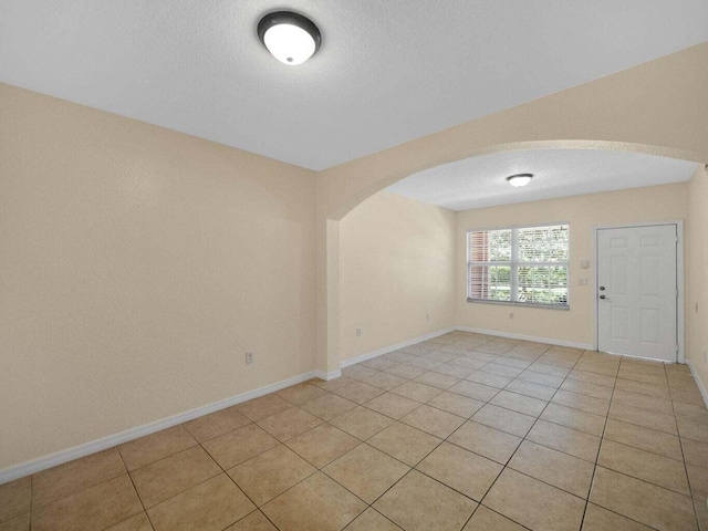 spare room with arched walkways, a textured ceiling, and light tile patterned floors