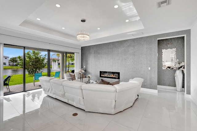 living area with an inviting chandelier, a glass covered fireplace, visible vents, a water view, and a raised ceiling