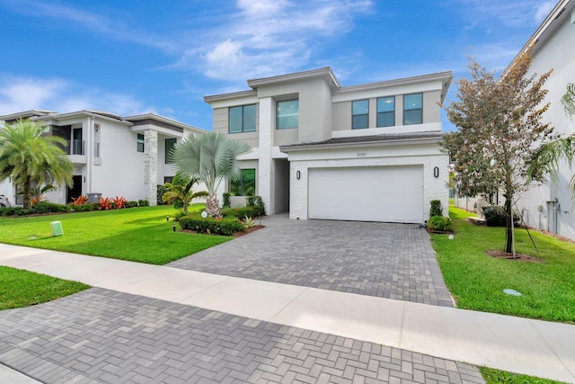 view of front of house with a front lawn, stucco siding, a garage, and decorative driveway
