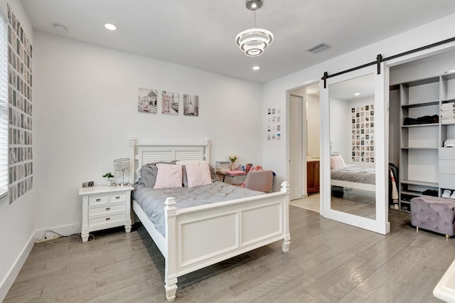bedroom featuring recessed lighting, a barn door, light wood finished floors, visible vents, and a spacious closet