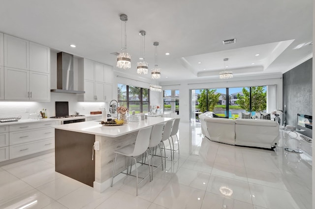 kitchen featuring a raised ceiling, visible vents, open floor plan, wall chimney range hood, and light countertops