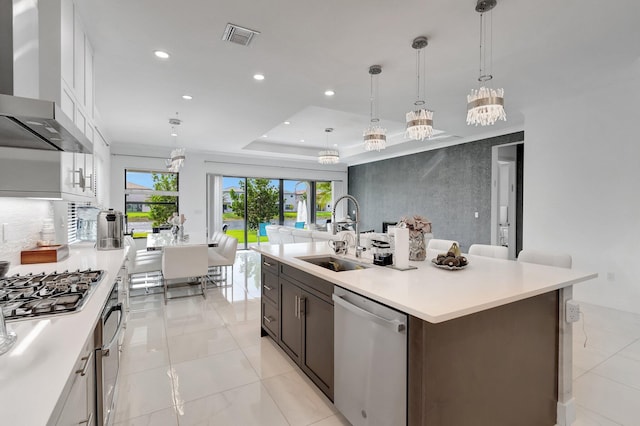 kitchen featuring light countertops, a sink, stainless steel appliances, visible vents, and wall chimney range hood