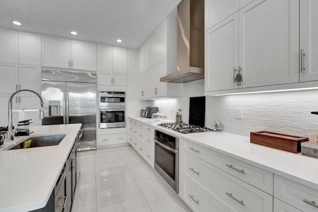 kitchen featuring a sink, wall chimney exhaust hood, light countertops, white cabinets, and appliances with stainless steel finishes