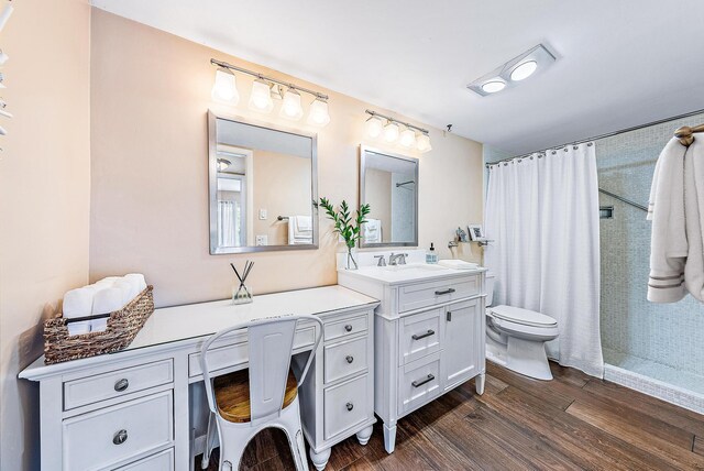 bathroom with vanity, wood finished floors, toilet, and tiled shower
