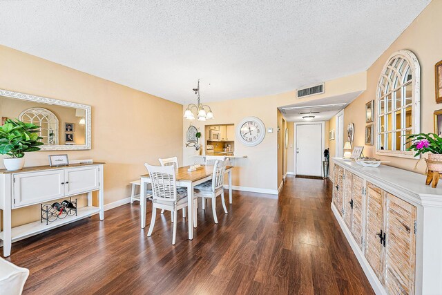 dining area with dark wood-style flooring, a textured ceiling, a chandelier, baseboards, and visible vents