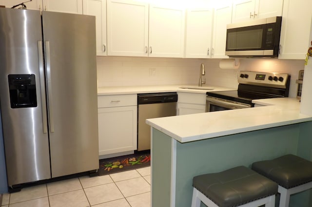 kitchen with backsplash, a kitchen bar, appliances with stainless steel finishes, a sink, and white cabinetry