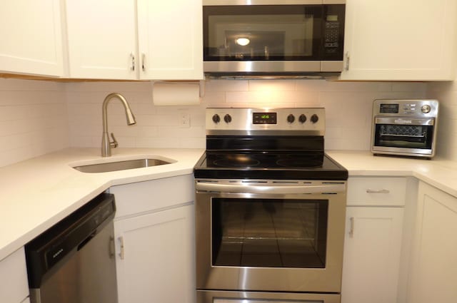 kitchen featuring light countertops, white cabinetry, a sink, appliances with stainless steel finishes, and backsplash