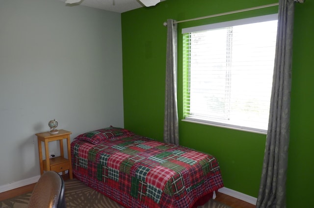 bedroom with baseboards, ceiling fan, wood finished floors, and multiple windows