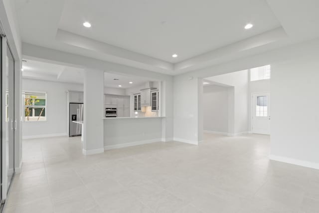 unfurnished living room featuring light tile patterned floors, a tray ceiling, and a wealth of natural light