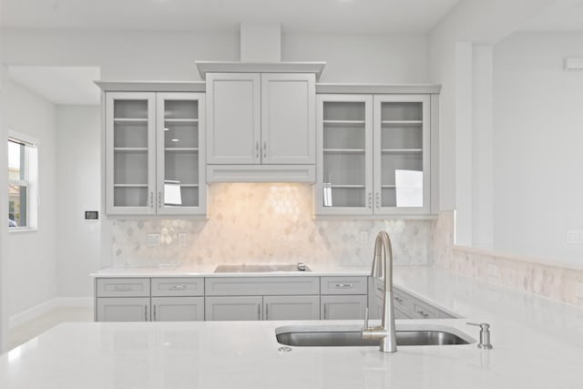 kitchen featuring a sink, decorative backsplash, black electric stovetop, and glass insert cabinets