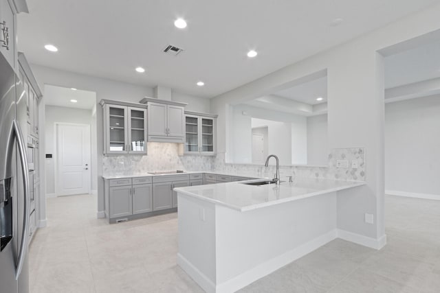 kitchen featuring a sink, a peninsula, backsplash, and glass insert cabinets