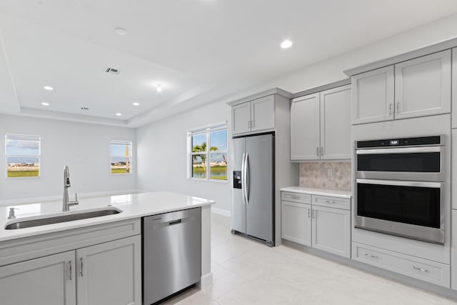 kitchen featuring appliances with stainless steel finishes, a sink, gray cabinets, a tray ceiling, and visible vents