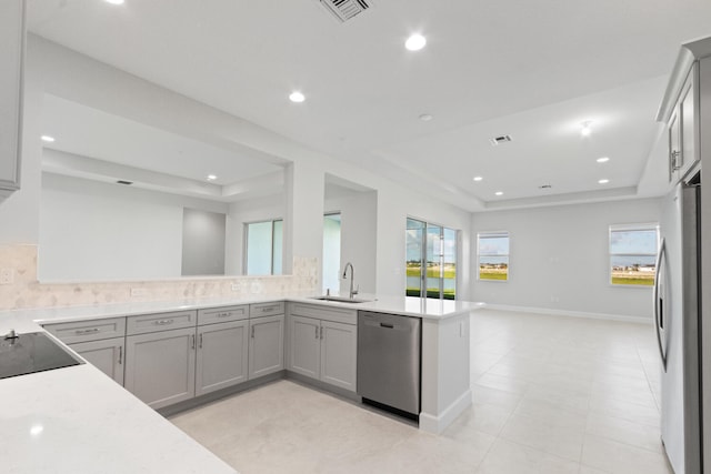 kitchen with a sink, gray cabinets, a tray ceiling, and stainless steel appliances