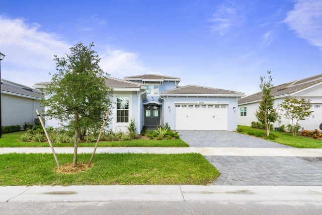 prairie-style home with an attached garage, a front lawn, stucco siding, decorative driveway, and french doors