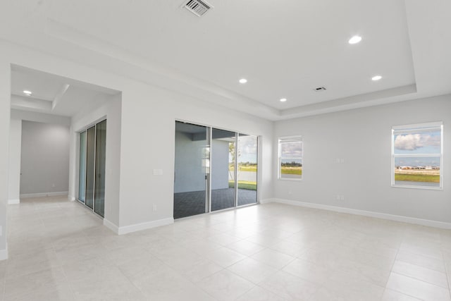 spare room with light tile patterned floors, baseboards, a tray ceiling, and visible vents