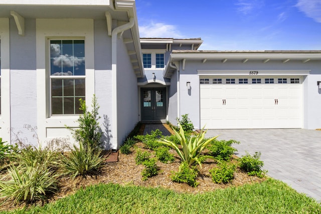 doorway to property featuring decorative driveway, a garage, stucco siding, and french doors