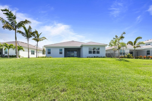 back of house with fence, stucco siding, a yard, and a tiled roof