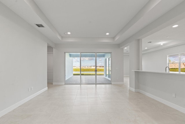 empty room featuring a raised ceiling, plenty of natural light, baseboards, and visible vents